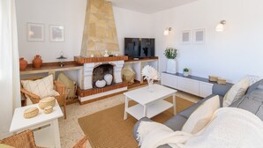 Una sala de estar con chimenea de piedra, muebles de mimbre, televisor de pantalla plana y sofá blanco.