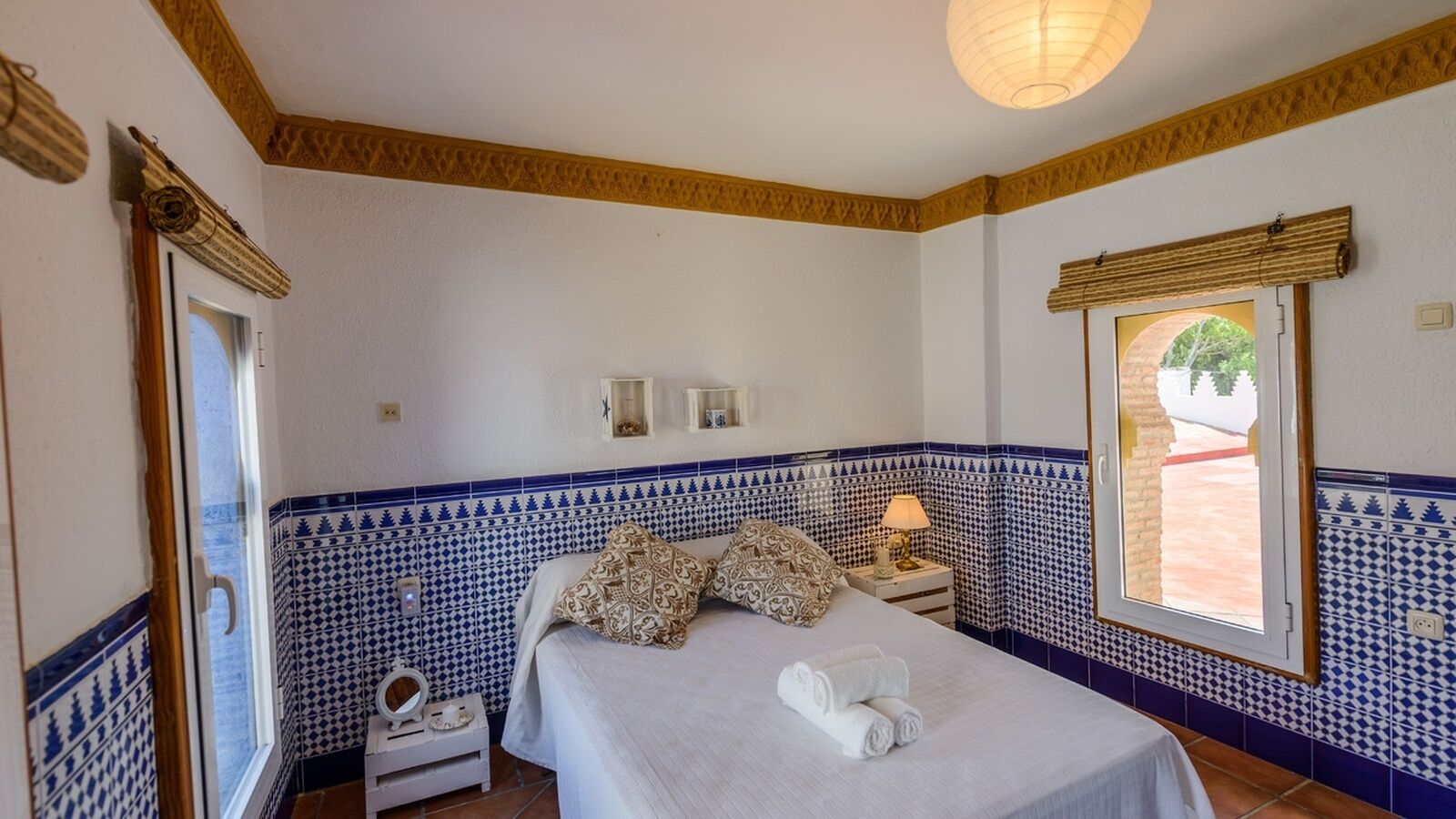 Une chambre à coucher avec un lit, une table de chevet, une lampe et une fenêtre donnant sur l’extérieur.