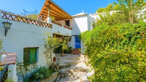A traditional white building with a wooden balcony, a blue door, and a stone pathway leading to a gate. - Casa Almijara Cómpeta by Ruralidays (Málaga)