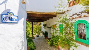 A narrow alleyway with a white wall, a blue sign reading "El Adarve", and a green door with decorative metalwork. - Casa Almijara Cómpeta by Ruralidays (Málaga)