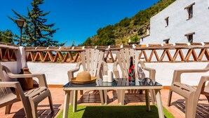 A terrace with outdoor seating, a table with a bottle and glasses, and a view of a hillside. - Casa Almijara Cómpeta by Ruralidays (Málaga)