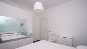 A bedroom with a bed, a chair, a nightstand, a dresser, a mirror, and a hanging light fixture. - S099 - Sirolo, new two-room apartment with wonderful sea view (Sirolo)