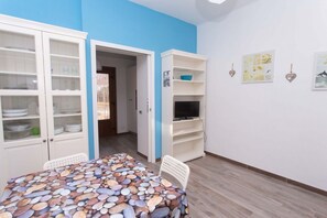 A room with a dining table, chairs, a TV stand, and a door leading to another room. - S099 - Sirolo, new two-room apartment with wonderful sea view (Sirolo)