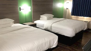 Ein Hotelzimmer mit drei Betten, jedes mit weißer Bettwäsche und Kopfteilen. An der Wand sind Leuchten befestigt und ein Fenster mit blauem Vorhang zu sehen.