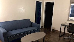 Ein Zimmer mit einem blauen Sofa, einem kleinen runden Tisch und einem Schreibtisch mit Stuhl.