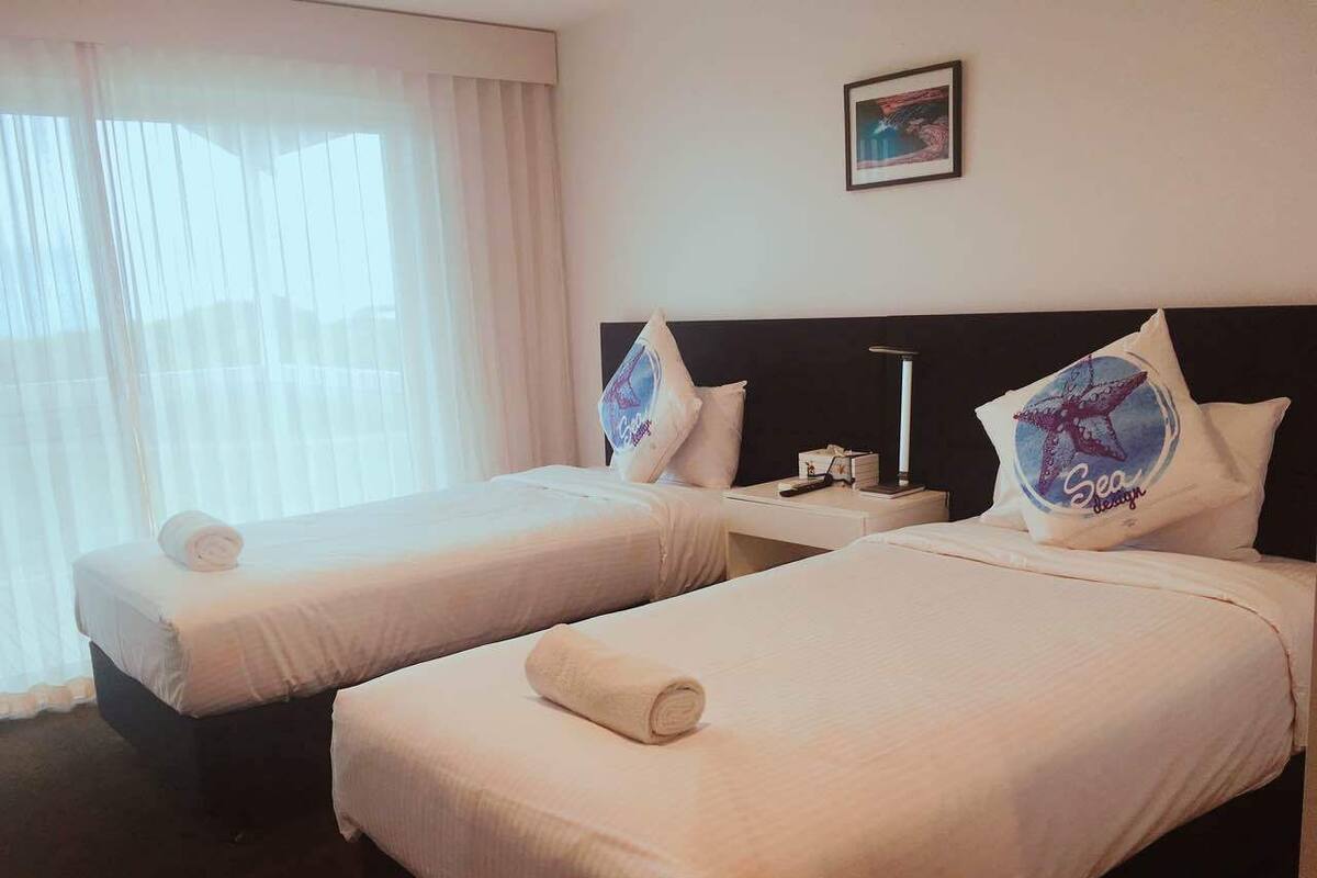 A hotel room with two beds, each with a pillow featuring a nautical design.