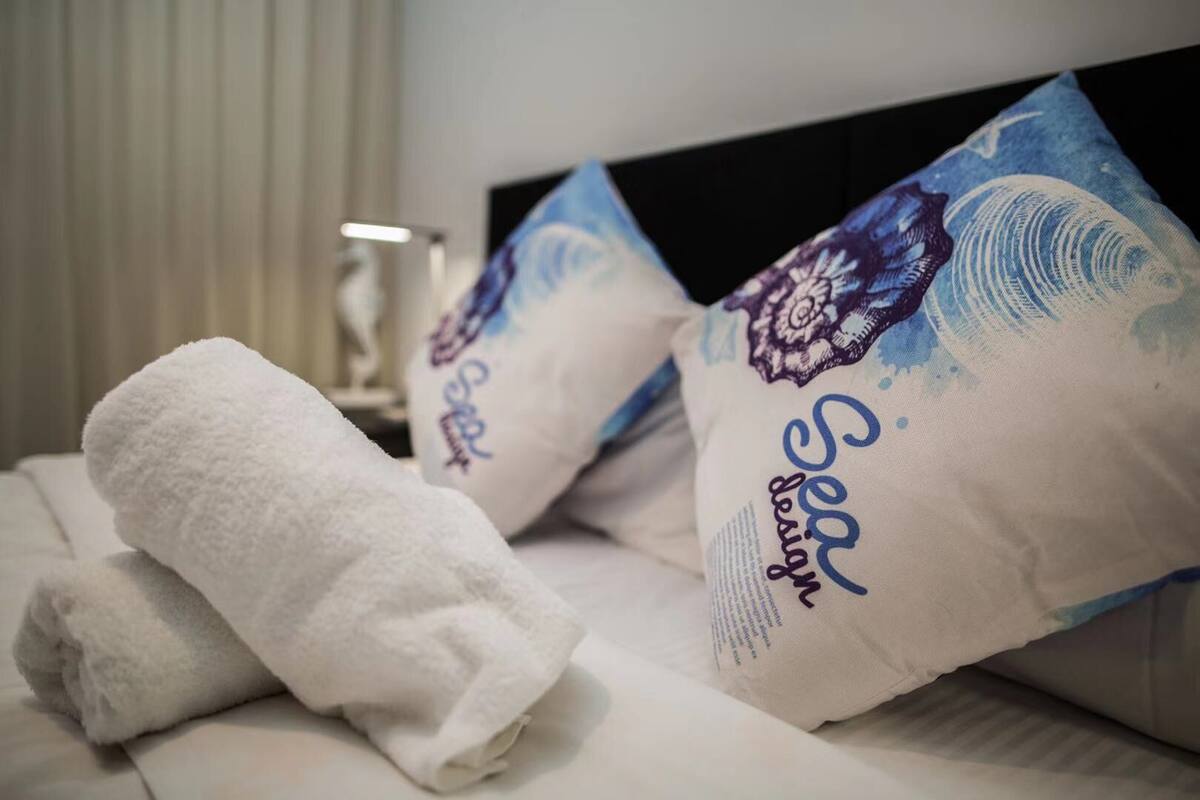 A neatly made bed with a folded white towel and two decorative pillows with a blue and purple design.