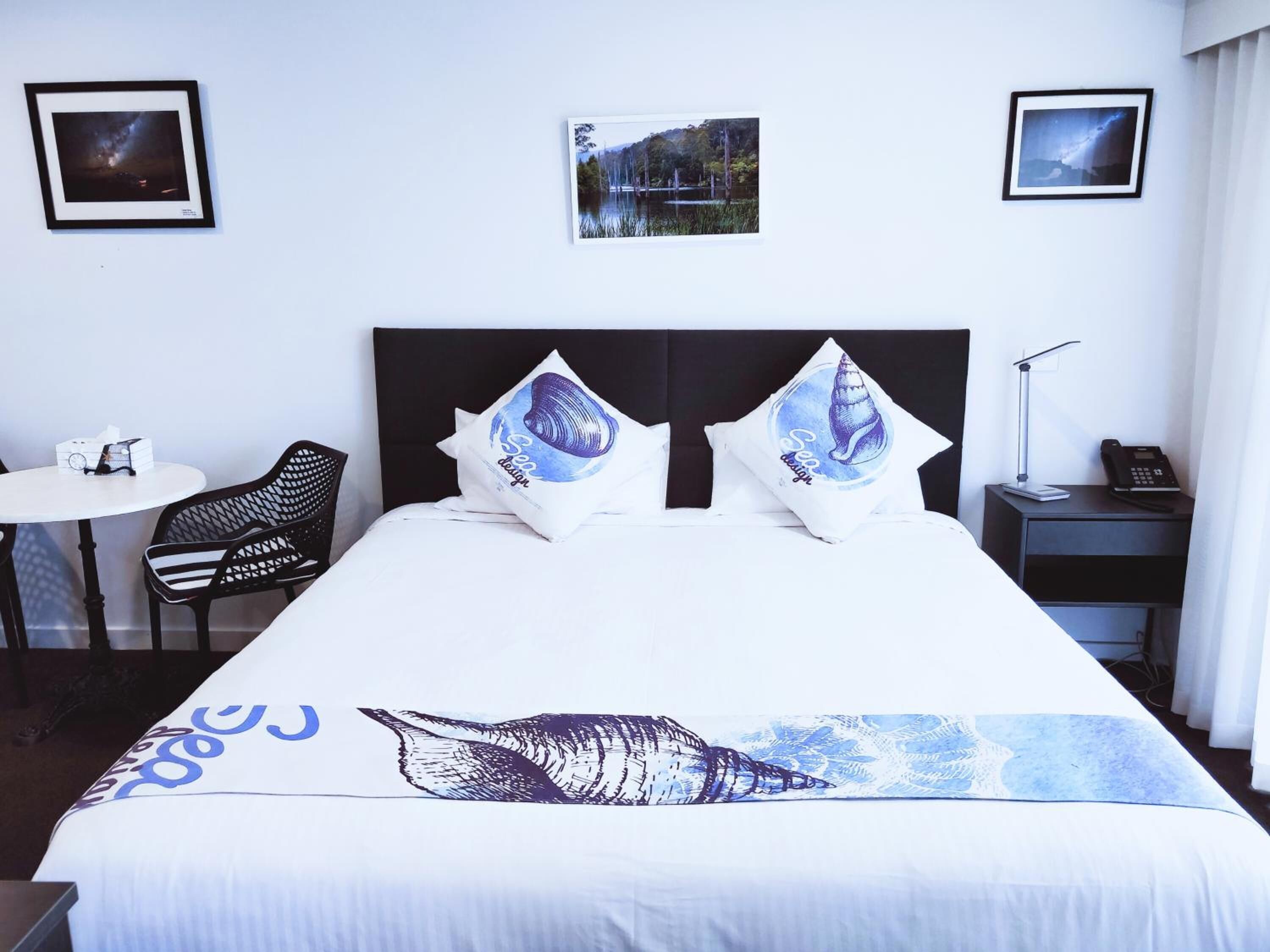 Una habitación de hotel con una cama, un escritorio, una silla y dos cuadros en la pared.
