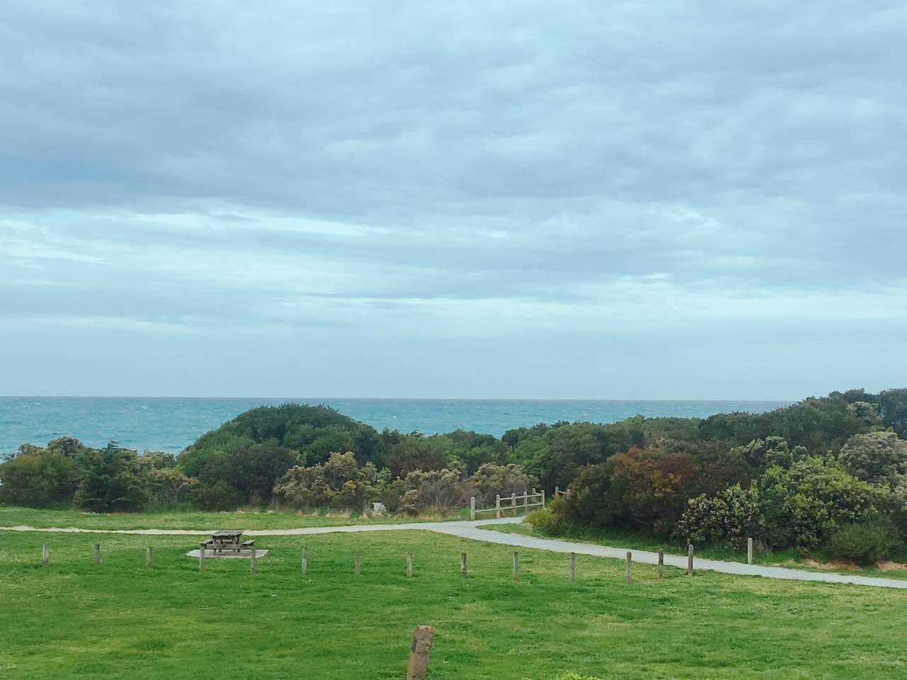 Un paysage côtier avec une zone herbeuse, un banc en bois et un sentier menant à la mer.