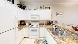A compact kitchen with white cabinets, a microwave, a stove, and a sink.