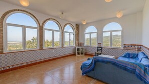 A spacious bedroom with large arched windows, a bed with a blue blanket, and a decorative wall with intricate tile work.