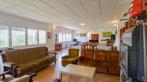 A spacious living room with a large sofa, armchairs, and a coffee table. There is a fireplace and a kitchen area in the background.