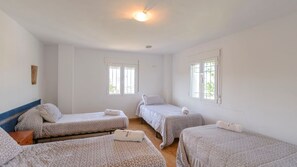 A room with three beds, each with a patterned bedspread and pillows, a wooden headboard, and a ceiling fan.