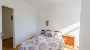 A bedroom with a bed, a wooden nightstand, a wall-mounted decoration, and a door leading to another room.