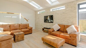 Ein geräumiges Wohnzimmer mit Ledersofas, einem Holztisch und einem an einer Ziegelwand montierten Fernseher.