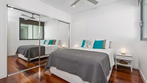 A modern bedroom with a large mirror, two beds, and a nightstand with a lamp. - OCEAN VIEWS @ NOR NOR EAST 201 (KINGSCLIFF)