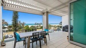 A balcony with a table and chairs, overlooking a beach and ocean. - OCEAN VIEWS @ NOR NOR EAST 201 (KINGSCLIFF)