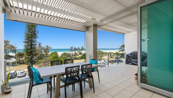 A balcony with a table and chairs, overlooking a beach and ocean. - OCEAN VIEWS @ NOR NOR EAST 201 (KINGSCLIFF)