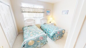 Quarto com duas camas de solteiro, uma janela com persianas, uma cadeira, mesa de cabeceira e abajur.