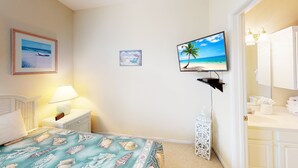 Une chambre à coucher comprenant un lit, une table de chevet, un téléviseur fixé au mur, et une salle de bain avec un lavabo et un miroir.