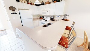 Une cuisine moderne avec des meubles blancs, un îlot central et un four à micro-ondes placé au-dessus de la cuisinière.
