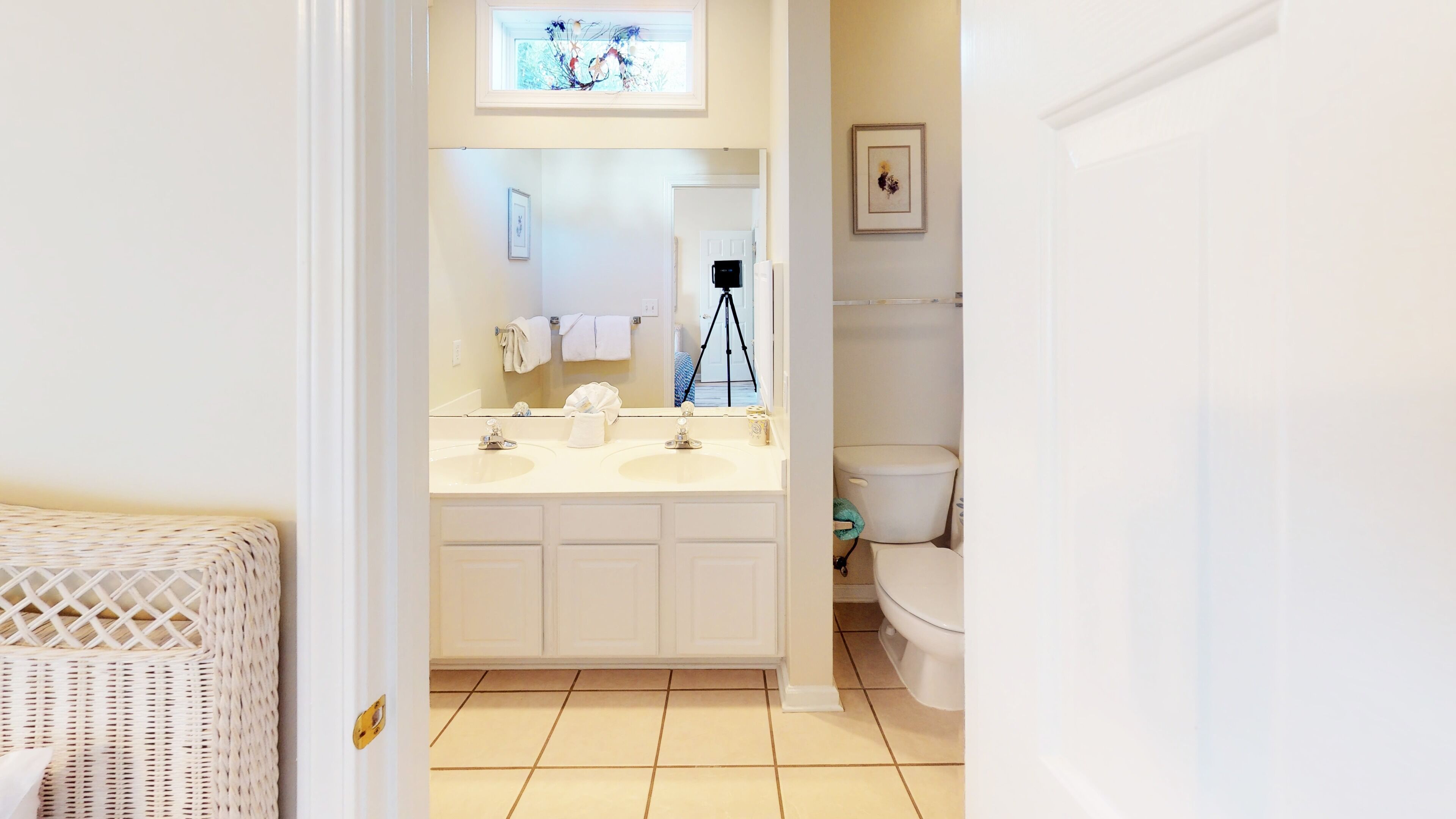 A bathroom with a white sink, mirror, and toilet. There is a tripod and a framed picture on the wall.