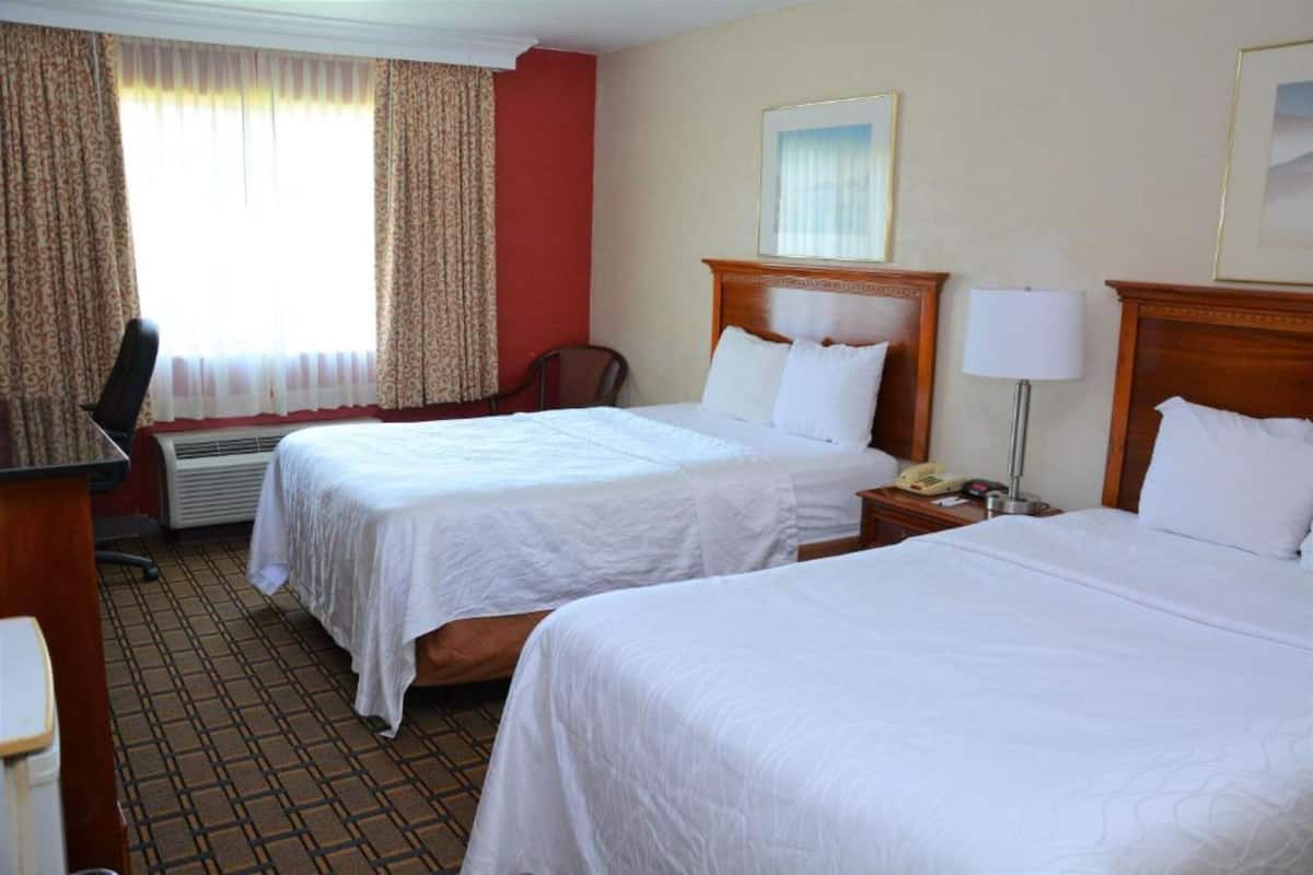 A hotel room with two beds, a desk, a chair, a lamp, and a window with curtains.