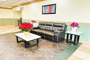 Um lobby com piso xadrez, um sofá de couro, uma mesa branca e dois vasos de flores.