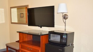 A hotel room with a flat-screen TV mounted on the wall, a microwave on a small table, a wooden dresser with drawers, a chair, and a lamp. - Buckeye Inn Express (Columbus)
