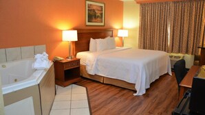 A hotel room with a large bed, two bedside lamps, a wooden headboard, a painting on the wall, a window with curtains, a desk, and a bathtub. - Buckeye Inn Express (Columbus)