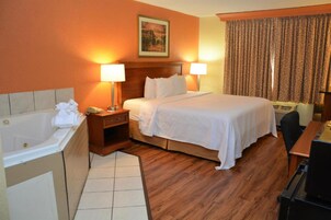 A hotel room with a large bed, two bedside lamps, a wooden headboard, a painting on the wall, a window with curtains, a desk, and a bathtub.