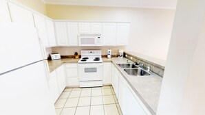 A compact kitchen with white cabinets, a microwave, a stove, and a sink.