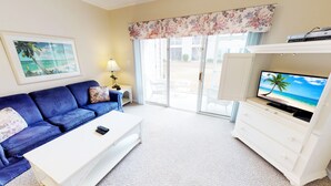 A living room with a blue sofa, white coffee table, and a TV displaying a beach scene.