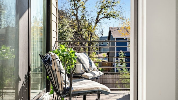 Een balkon met een stoel en een kleine tafel, met uitzicht op een woongebied met bomen en huizen.