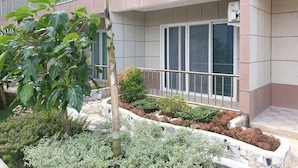 Um edifício moderno com varanda, paredes revestidas de azulejos e um jardim ajardinado com diversas plantas.