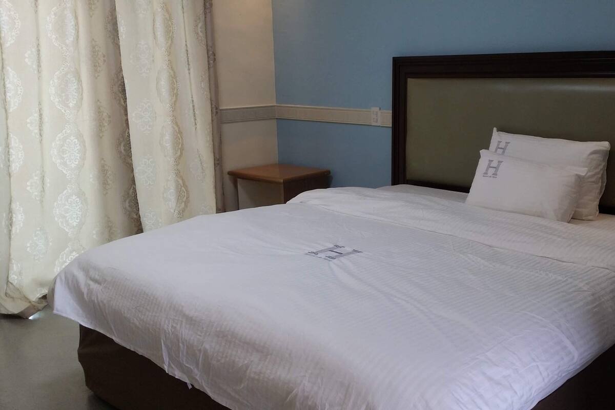 A neatly made bed with a white bedspread and pillows, a wooden nightstand, and a blue wall with a white baseboard.