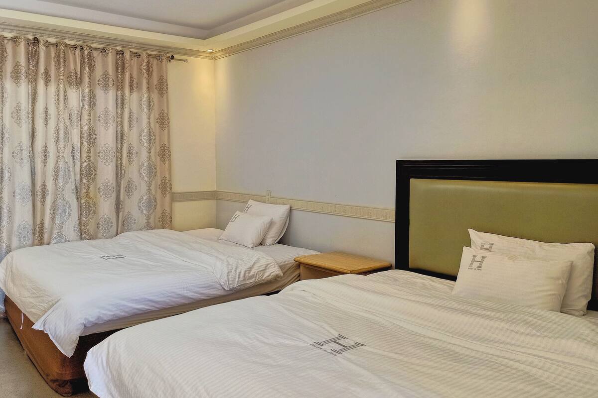 A hotel room with two single beds, a wooden nightstand, and a headboard with a logo.