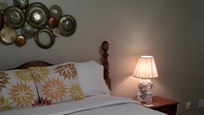 Ein ordentlich bezogenes Bett mit floralem Bettzeug, ein hölzerner Kopfteil, eine Nachttischlampe und Wanddekoration.