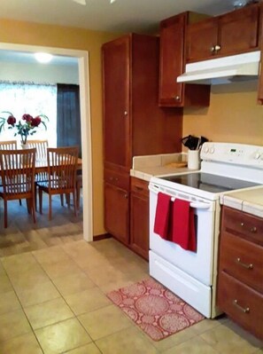 A kitchen with wooden cabinets, a white stove, and a dining area with chairs and a table. - House  Perfect For Short/Long Term Stays! (Chewelah)