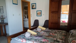 Un dormitorio con colcha estampada de flores, dos sillas, una puerta de madera y un baño visible a través de una puerta abierta.