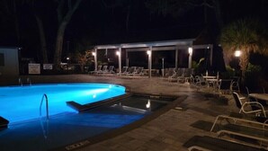Uma piscina à noite com espreguiçadeiras e um espaço coberto para sentar.