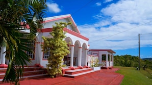 A building with a red and white facade, arched windows, and a covered porch. - Sunny Palm Villas (Laborie)