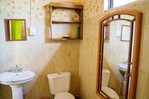 Een badkamer met een toilet, twee wastafels, een spiegel en een plankje met een groene vaas.