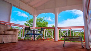 A covered outdoor area with a wooden deck, a sofa, a table with chairs, and a bench. - Sunny Palm Villas (Laborie)