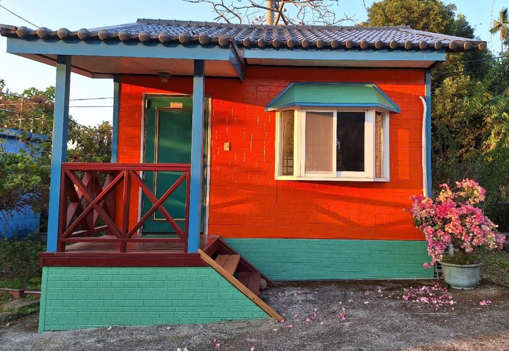 A small, colorful house with a red and green exterior, a window, and a porch with a railing.