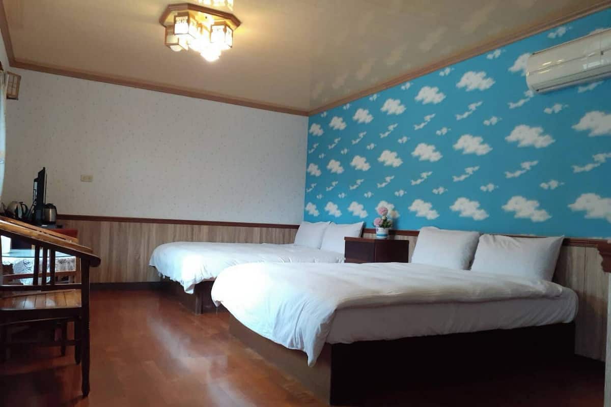 A hotel room with two beds, a wooden desk, a nightstand, and a wall with a cloud pattern.