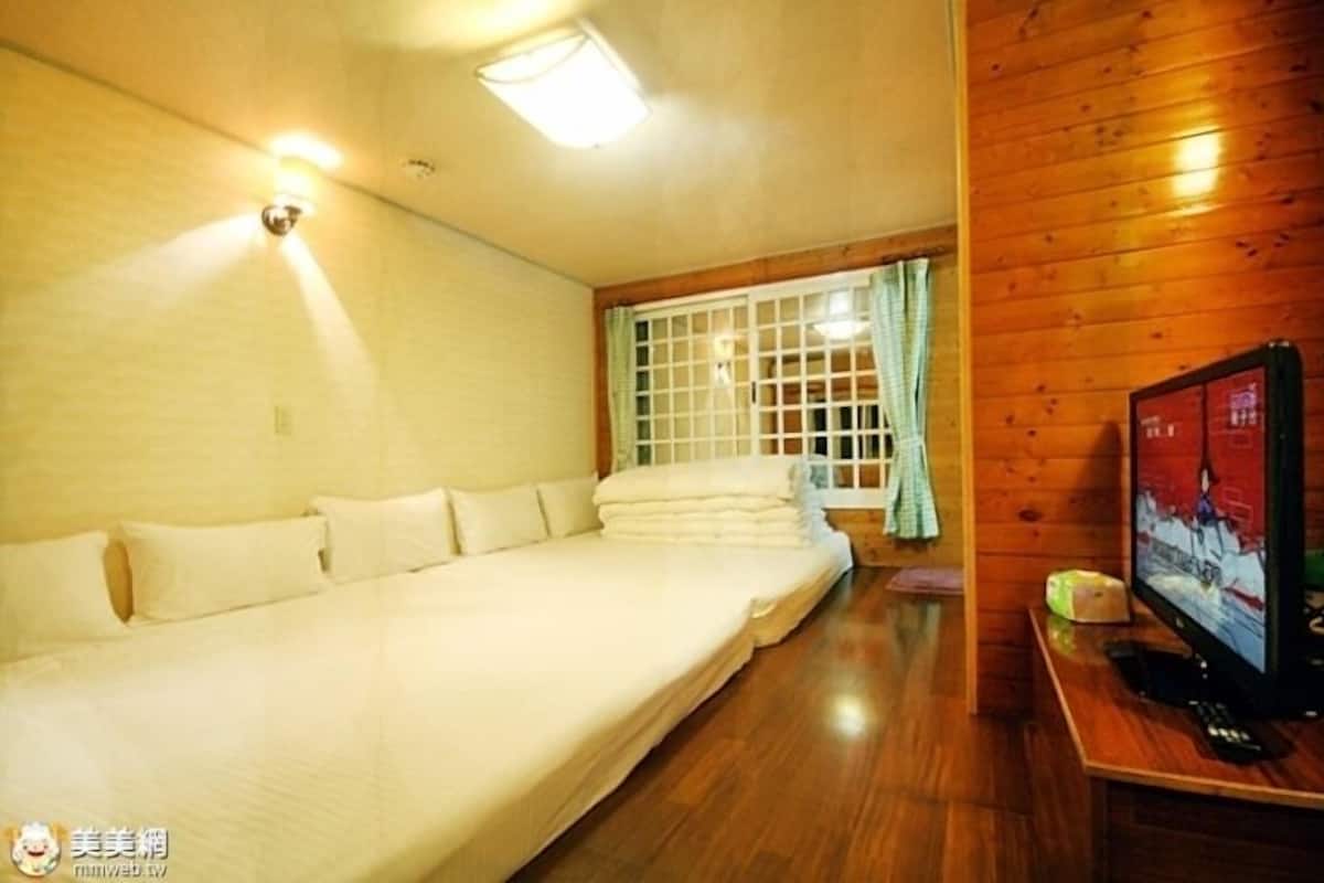 A room with a large bed, a television on a wooden stand, and a window with curtains.