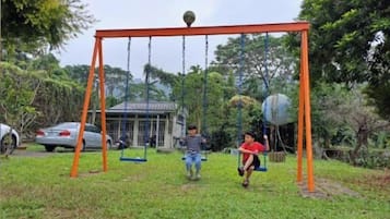 A swing set in a grassy area with trees and a building in the background.