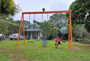 A swing set in a grassy area with trees and a building in the background. - Xiangcun Homestay (Gukeng)