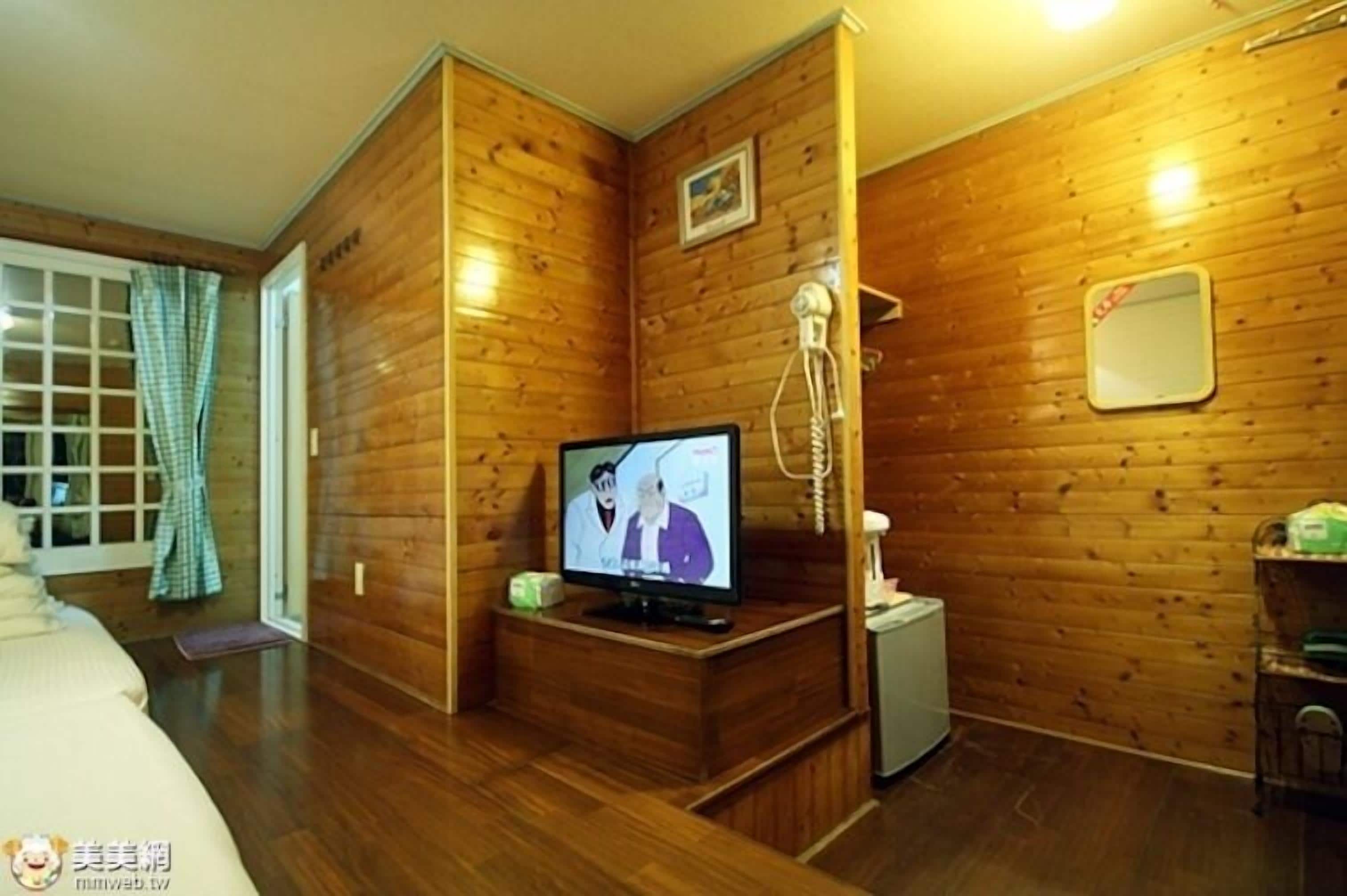 A wooden-paneled room with a television, a small table, and a chair.